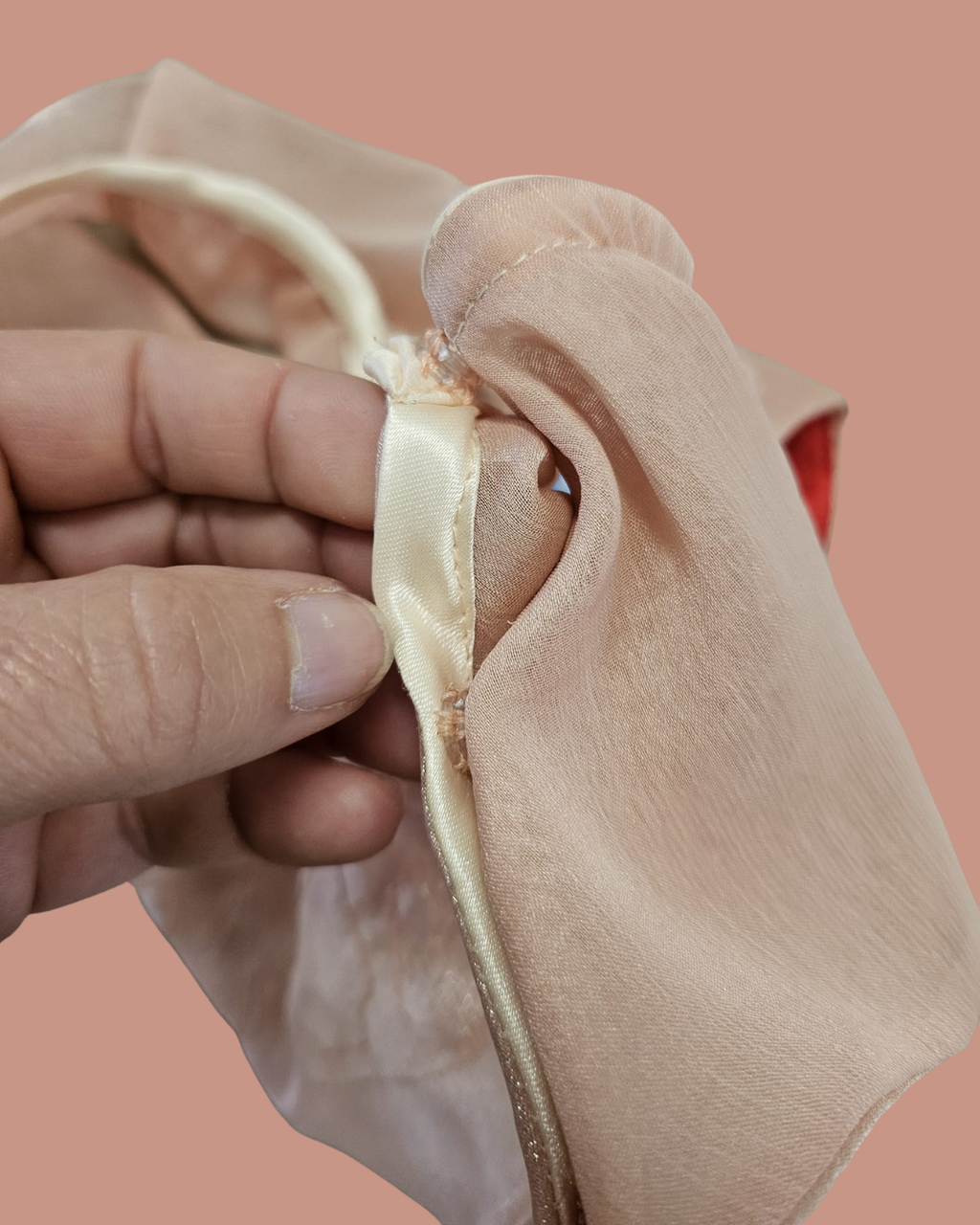 Close-up of a hand holding a beige fabric with a pink background