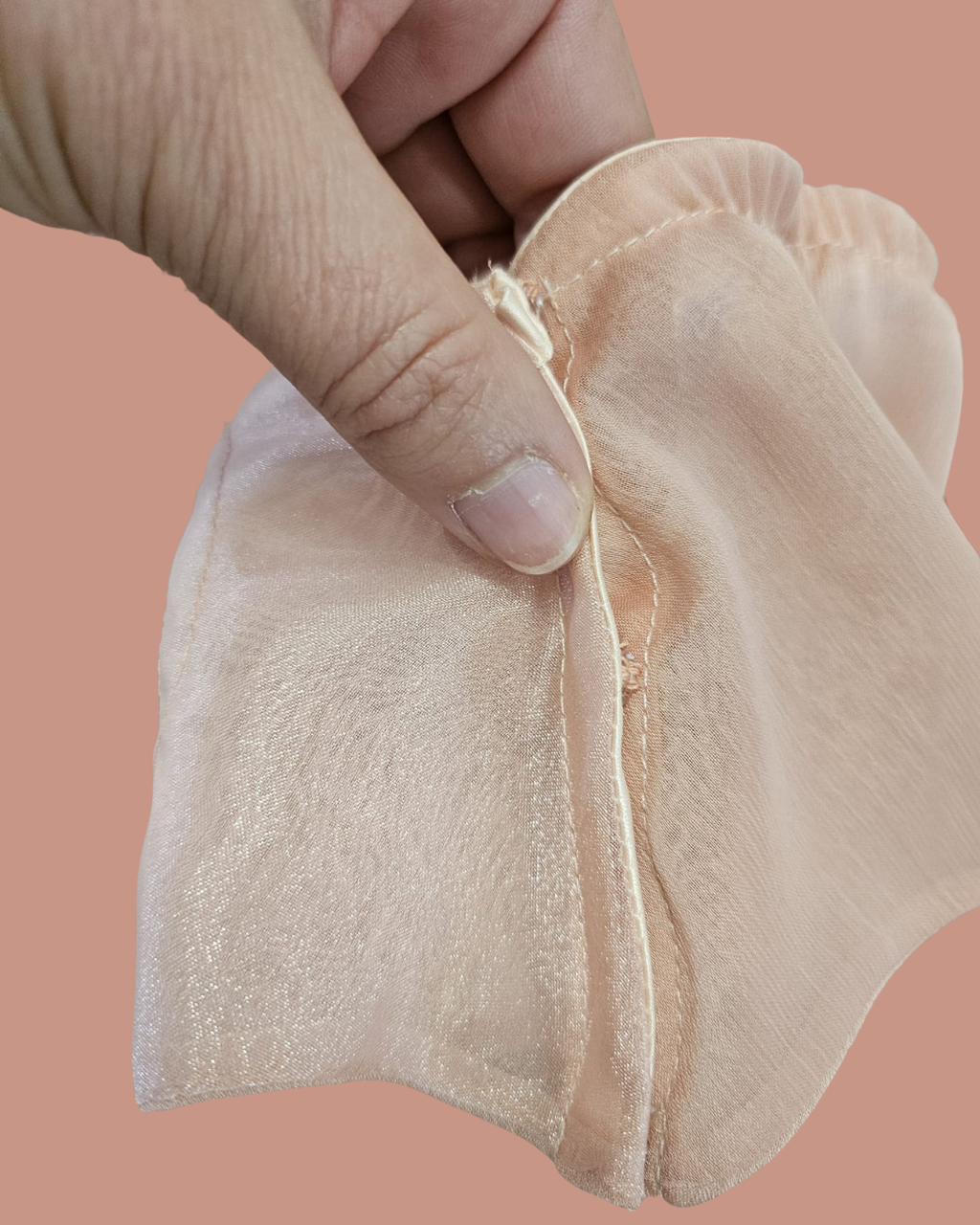 Close-up of a hand holding a beige fabric item against a pink background