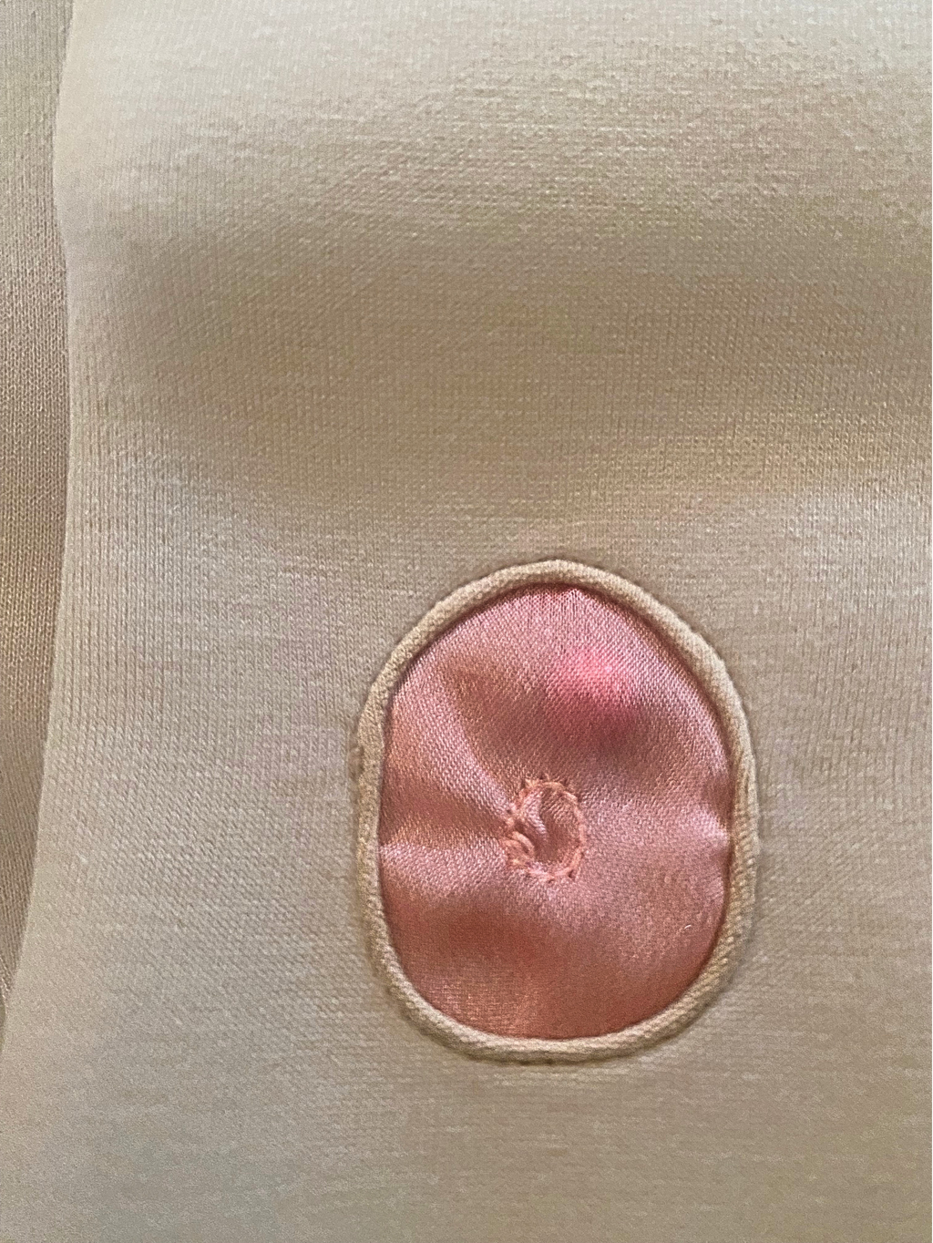 Close-up of a beige fabric with a pink circular patch on a white background . Inside a red like pearl