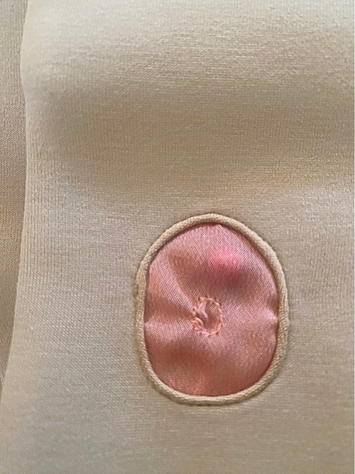 Close-up of a beige fabric with a pink circular patch on a white background . Inside a red like pearl